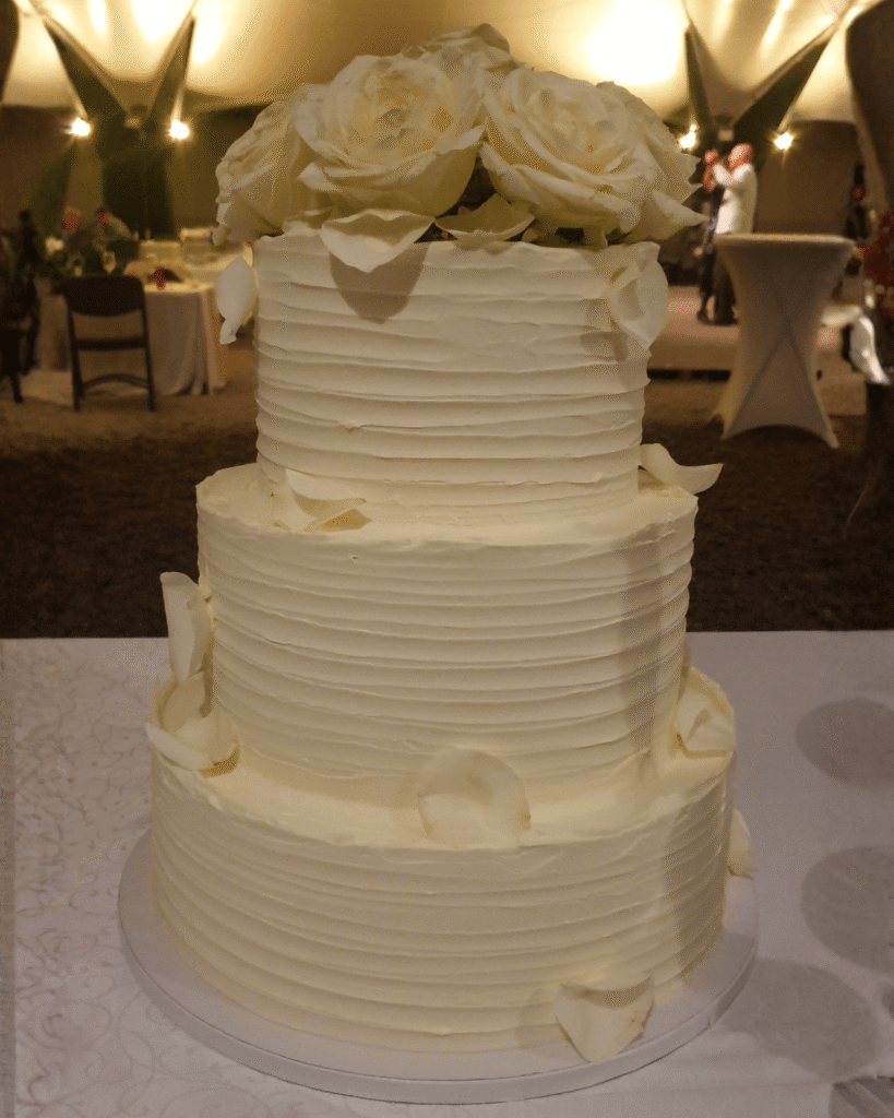 Elegantna večnadstropna poročna torta Taca z belim premazom in velikimi kremnimi vrtnicami na vrhu.